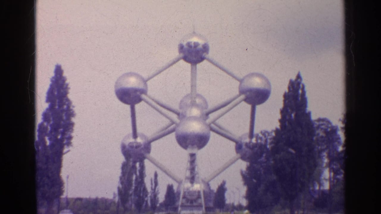 1961 8mm view of the Atomium in Brussels, framed by trees and a pale sky.