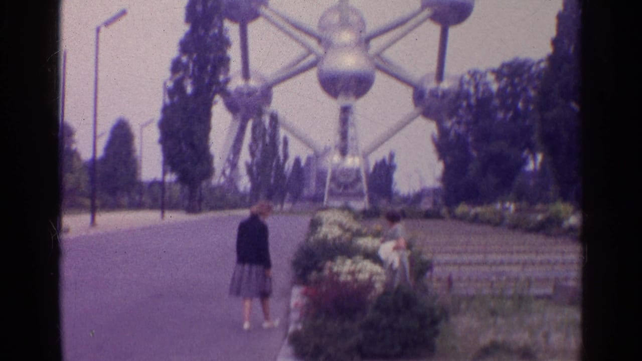 Visitors near flowerbeds with the Atomium rising behind a paved path.