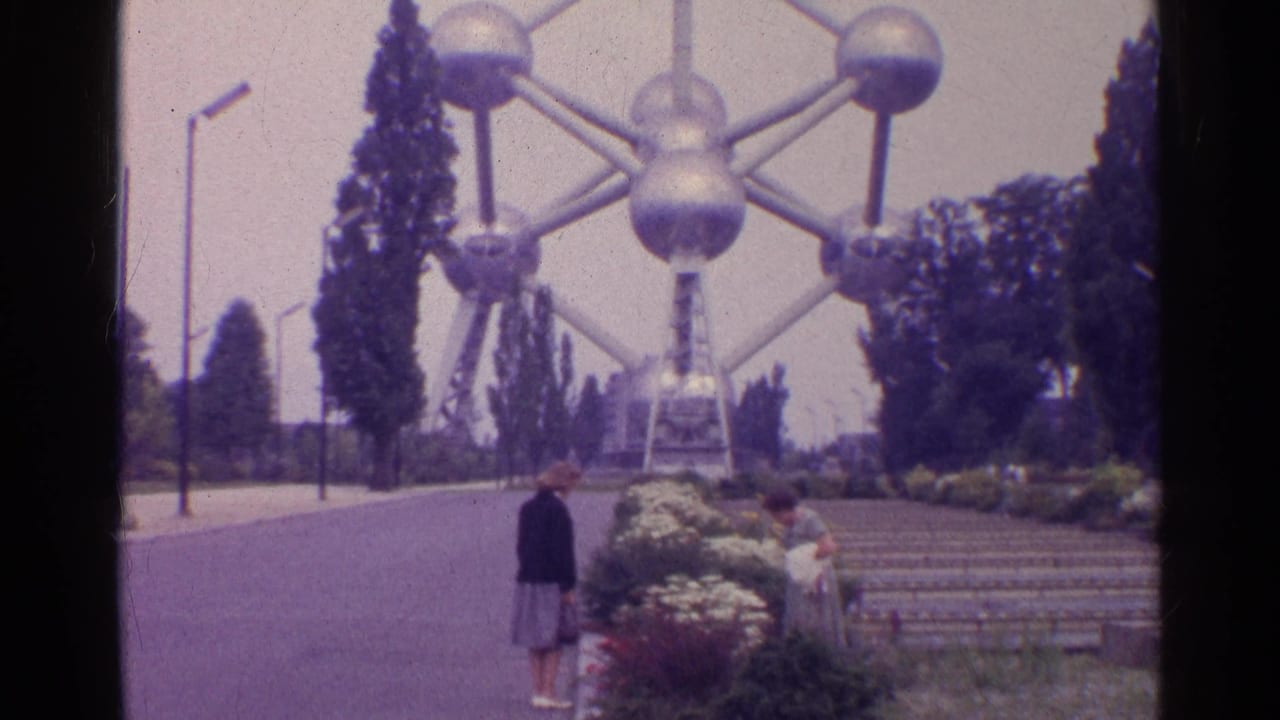 A woman stands on the paved approach while another person is near the flowerbeds below the Atomium in 1961 home-movie footage.