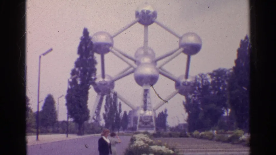 The Atomium fills the background above a garden approach, with two visitors visible in the lower frame on 8mm film.