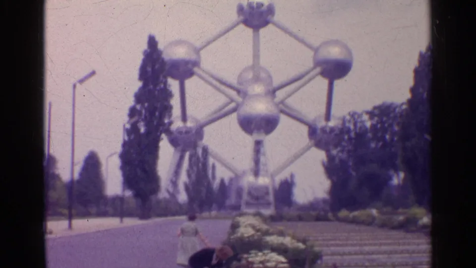 A visitor bends beside flowers in the foreground while the Atomium, trees, and steps remain prominent behind them.