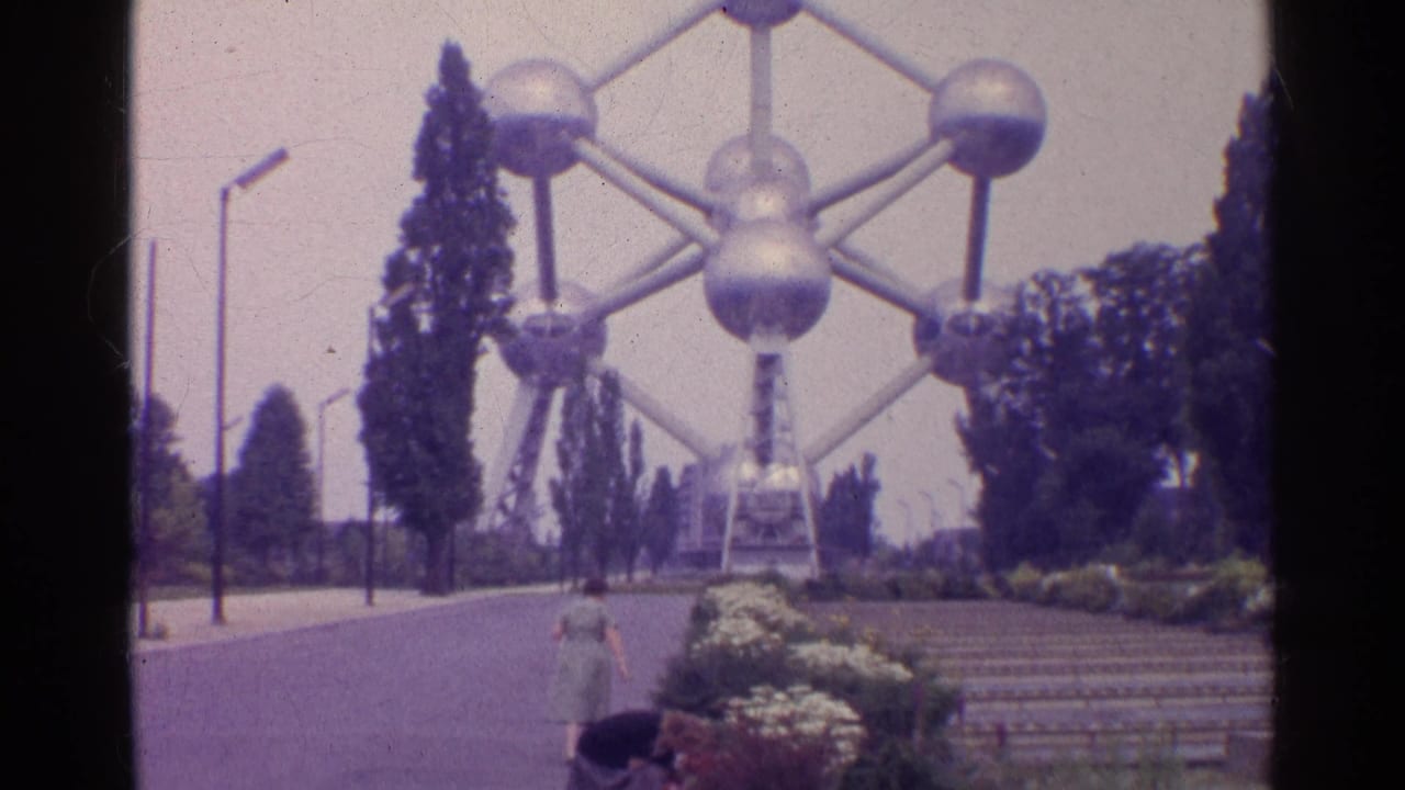Large metal sphere-and-tube landmark beside trees, walkway, flower beds, and a woman in the foreground.