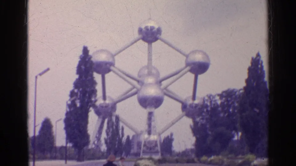 The 8mm frame shows the sphere-and-tube structure looming over trees and paths, with small visitors near the lower edge.