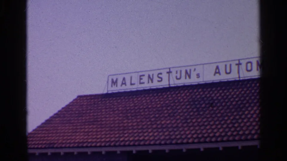 Final 8mm frame briefly shows a red tiled roof and a partial rooftop business sign reading MALENSTUN's AUTOM.