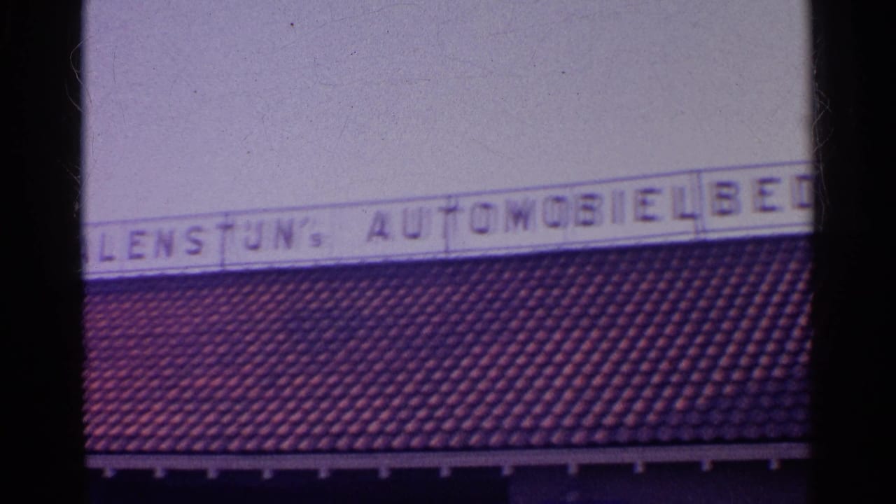 Cropped automobile business sign above a red tiled roof, framed by dark vertical film edges.