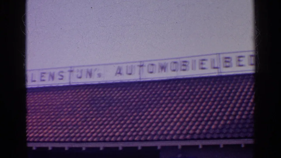 Close 8mm view of block-letter automobile business signage over roof tiles, likely from the same European dealership exterior.