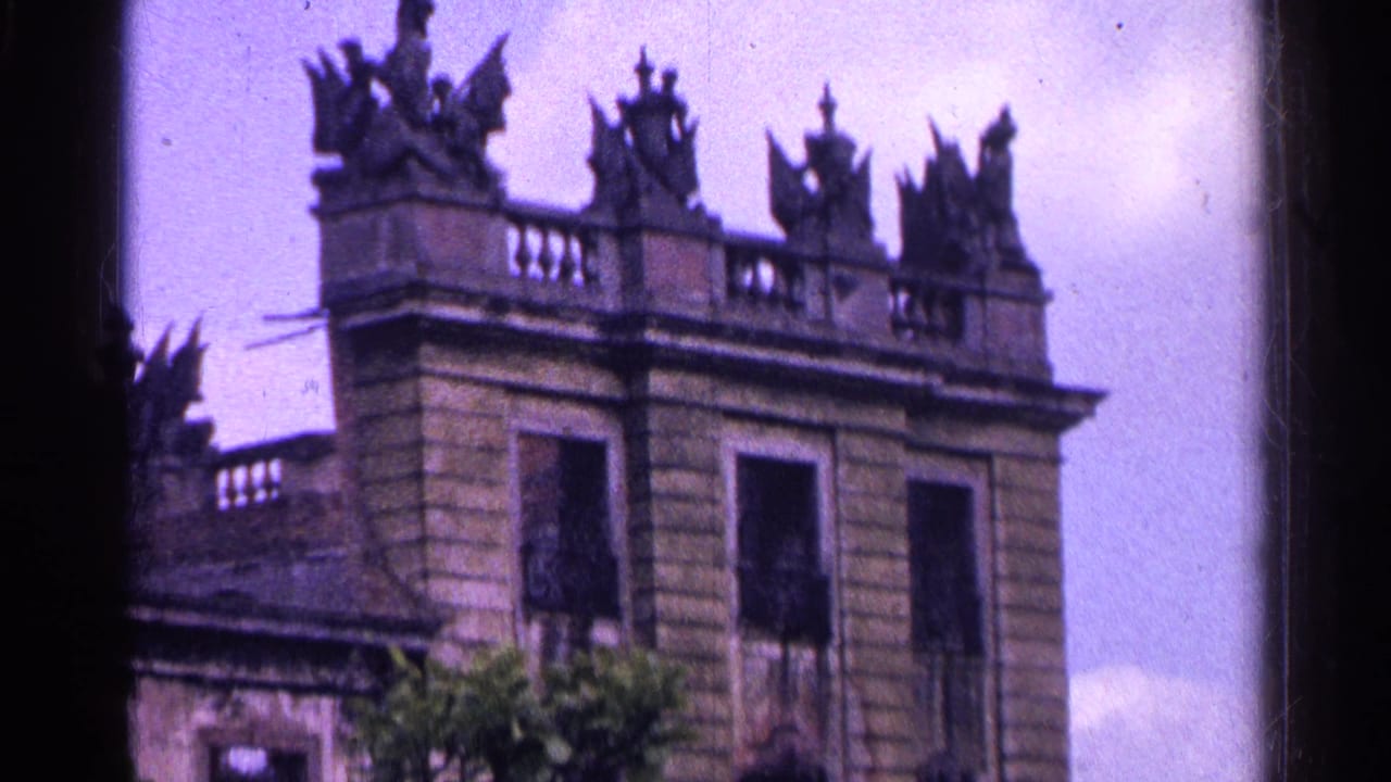 1961 Switzerland 8mm frame showing the upper portion of an ornate historic stone building with statues or gargoyles along the roofline.