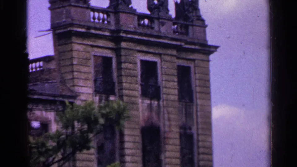 1961 Switzerland travel-film frame with carved roof figures, a balustrade, and the upper facade of an old stone building.