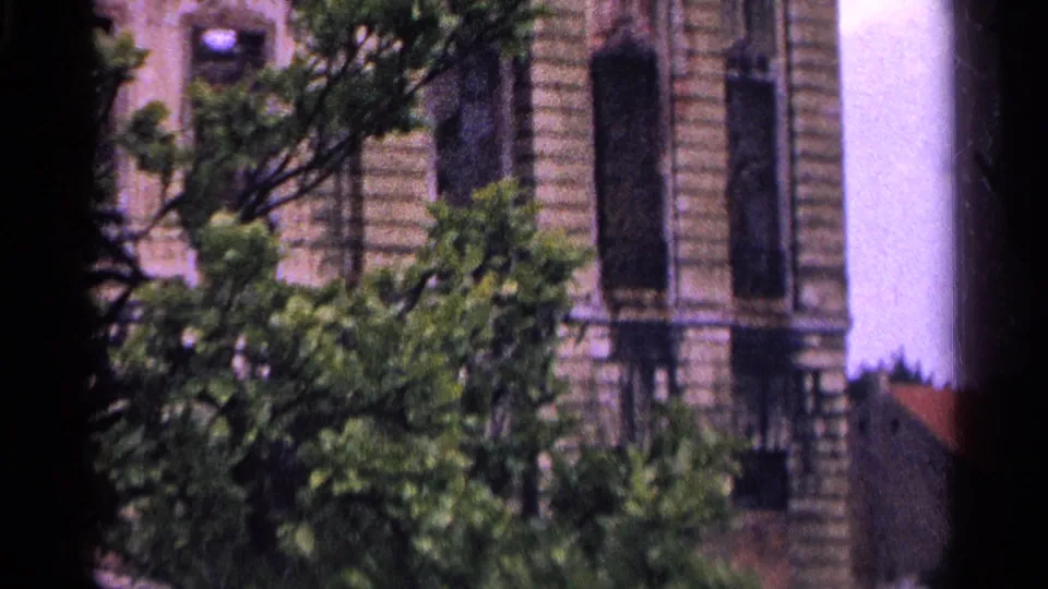 1961 Switzerland 8mm frame showing a weathered ornate building facade partly obscured by trees and film gate shadows.