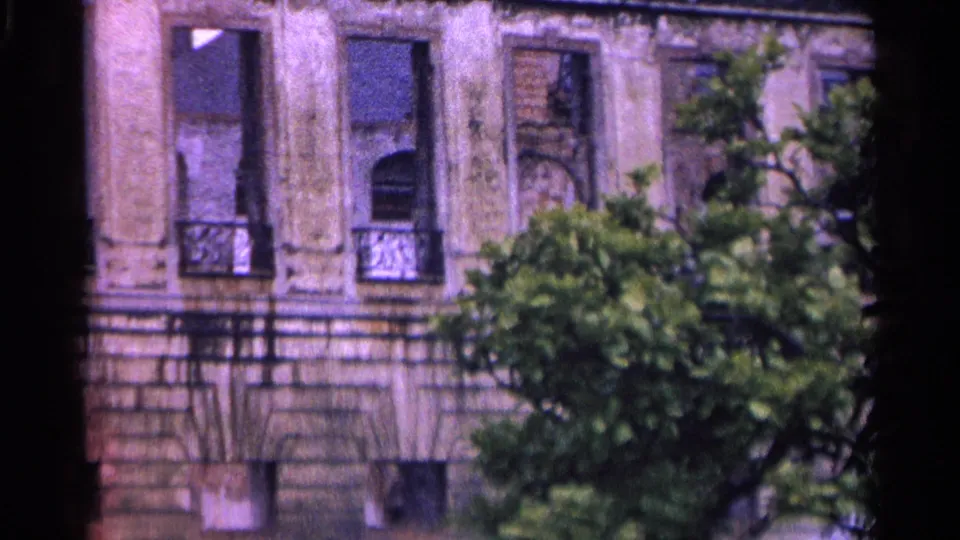 1961 Switzerland 8mm close view of damaged or open windows, balcony railings, and aged stonework behind leafy trees.