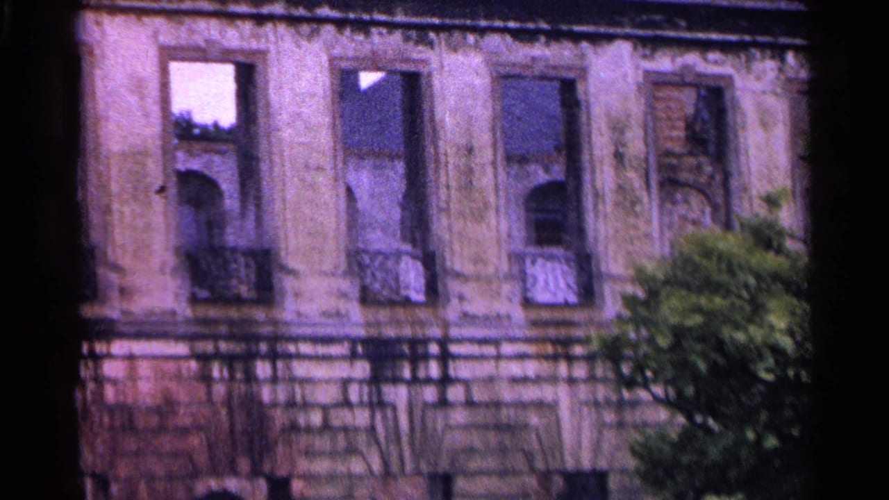 1961 Swiss 8mm frame showing an aged building facade with arched windows, ornate balcony railings, and foliage at the edge.