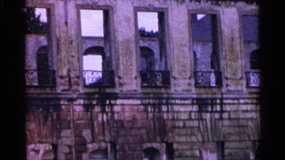 1961 Swiss home-movie frame of an older urban facade with tall windows, arched openings, and decorative balcony rails.