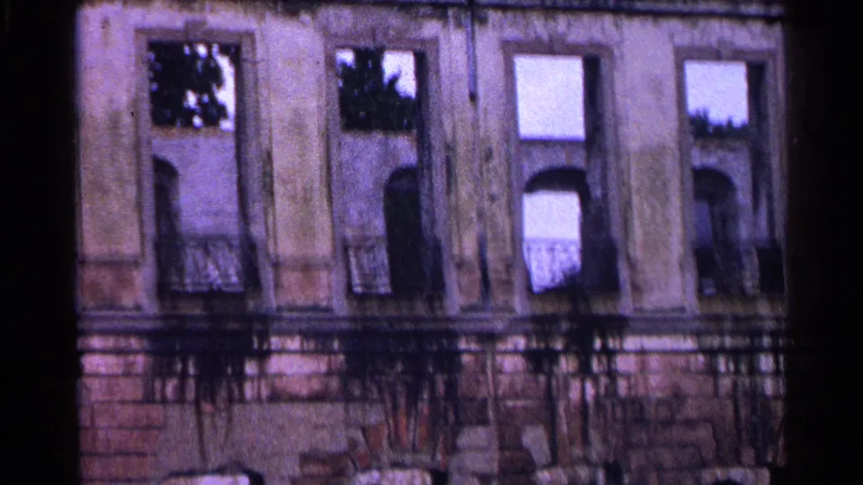 Vintage 8mm frame from Switzerland in 1961 showing a worn building facade with window bays, balconies, and foliage reflections.