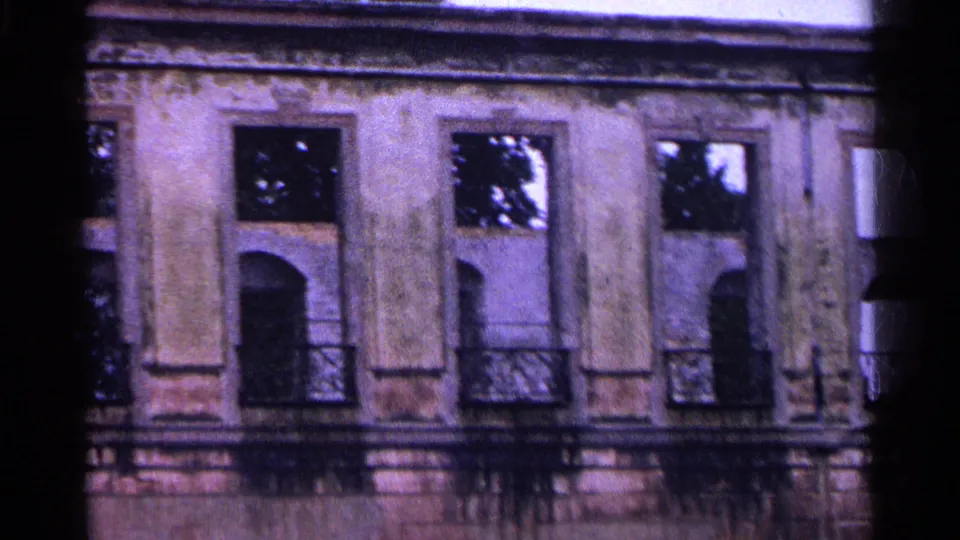 1961 Swiss 8mm frame showing a weathered facade section with arched windows, balcony railings, and soft film exposure.
