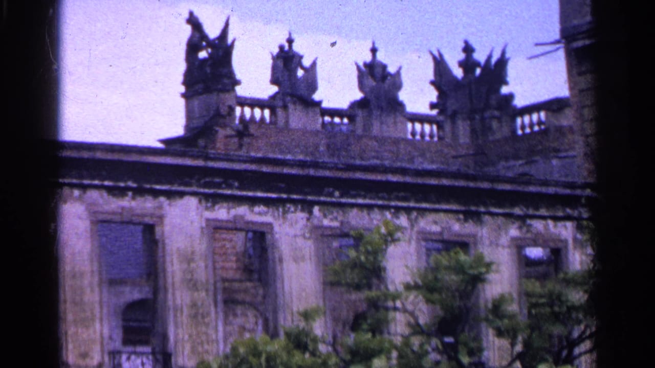 Ornate roofline with statues above a worn facade and trees below.