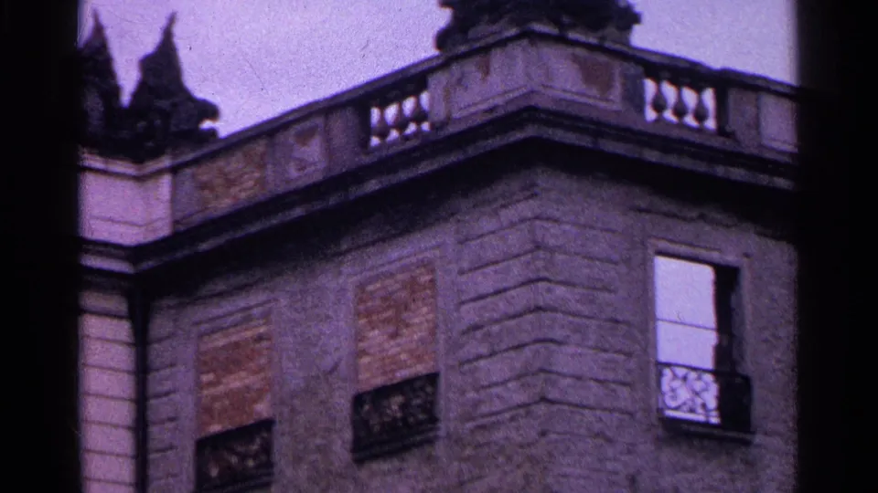 1961 Switzerland 8mm frame showing a weathered stone building corner with boarded openings, iron window guards, and an ornate roof balustrade.