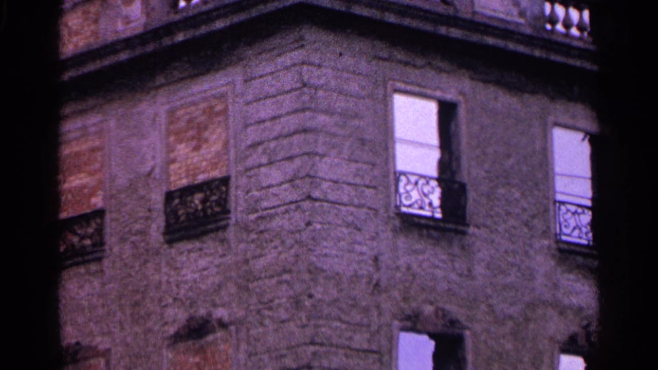 Closer view of a stone facade with white windows, iron railings, and boarded openings.
