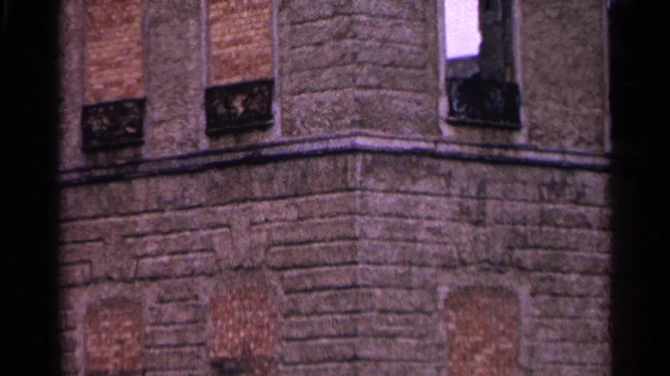 1961 Switzerland 8mm frame showing a weathered corner facade with boarded windows, iron railings, white window openings, and layered stone courses.