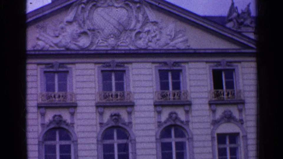 1961 Swiss 8mm frame with sculpted roofline relief, decorative trim, upper windows, and balcony railings.