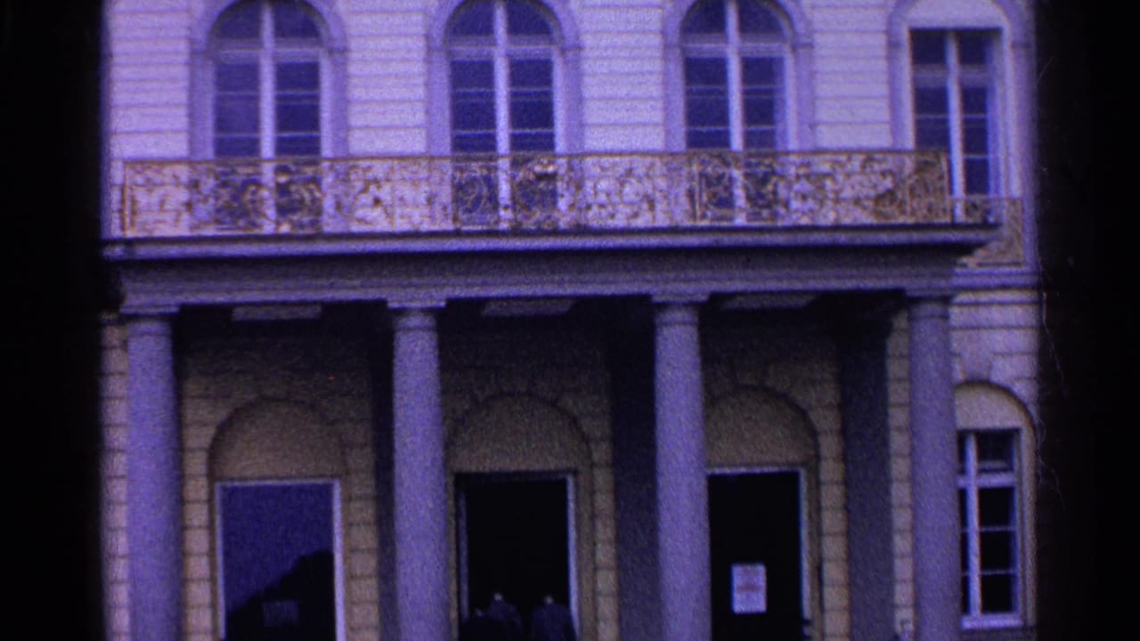 1961 Switzerland home-movie view of the lower facade, showing classical columns, a balcony, arched openings, and shadowed entrances.