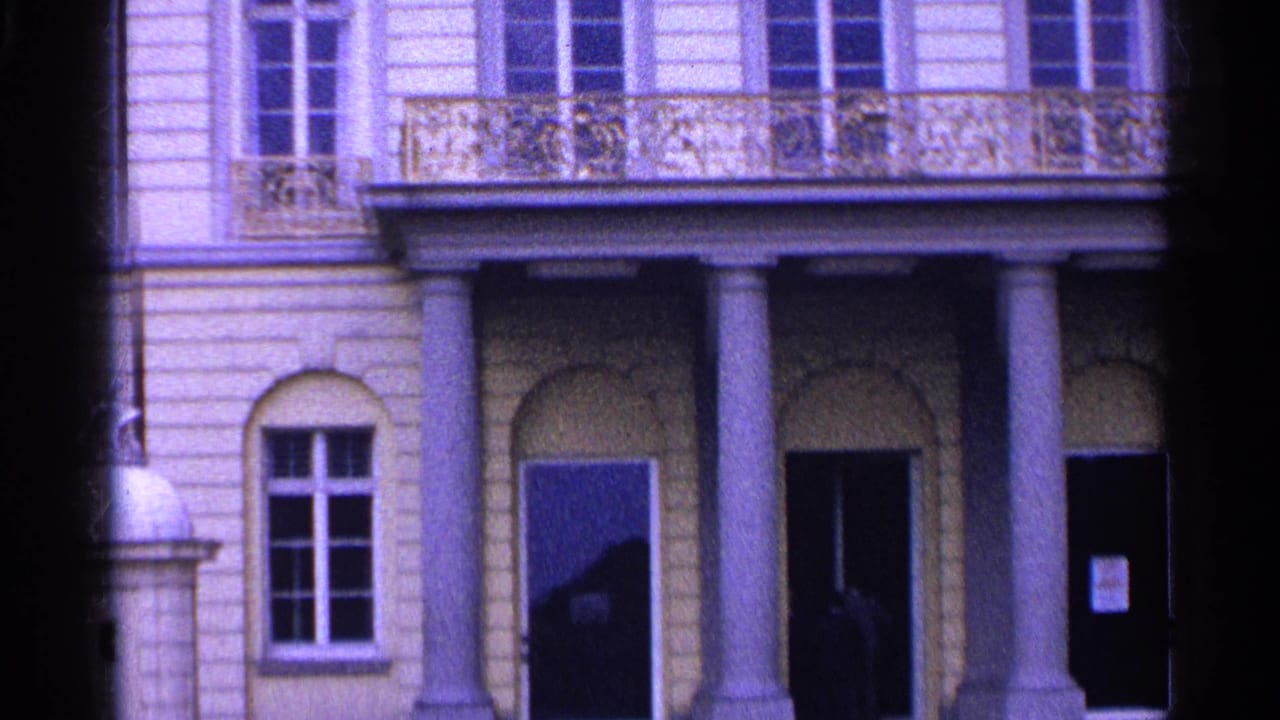 1961 Switzerland frame showing a columned entrance area, balcony railings, arched ground-floor openings, and tall upper windows.