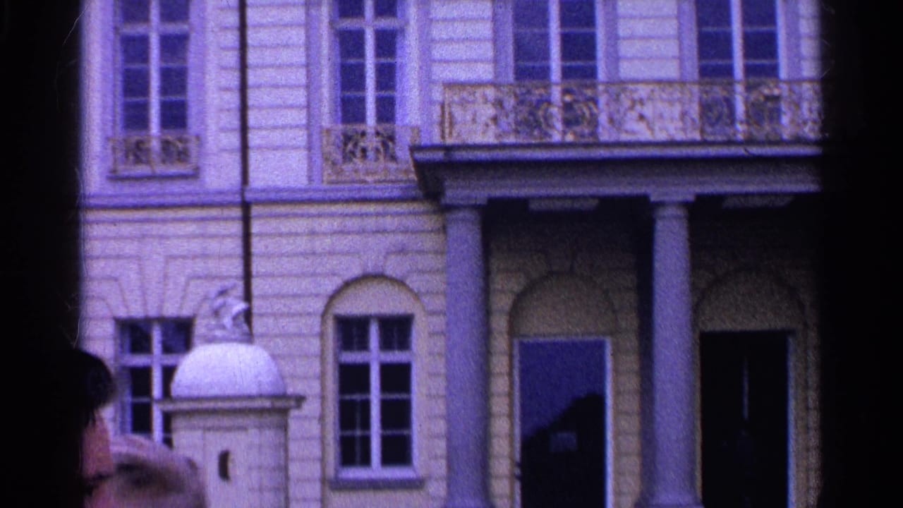 1961 Switzerland 8mm frame showing a formal building entrance with columns, balcony railing, and a partly cropped person at the edge.