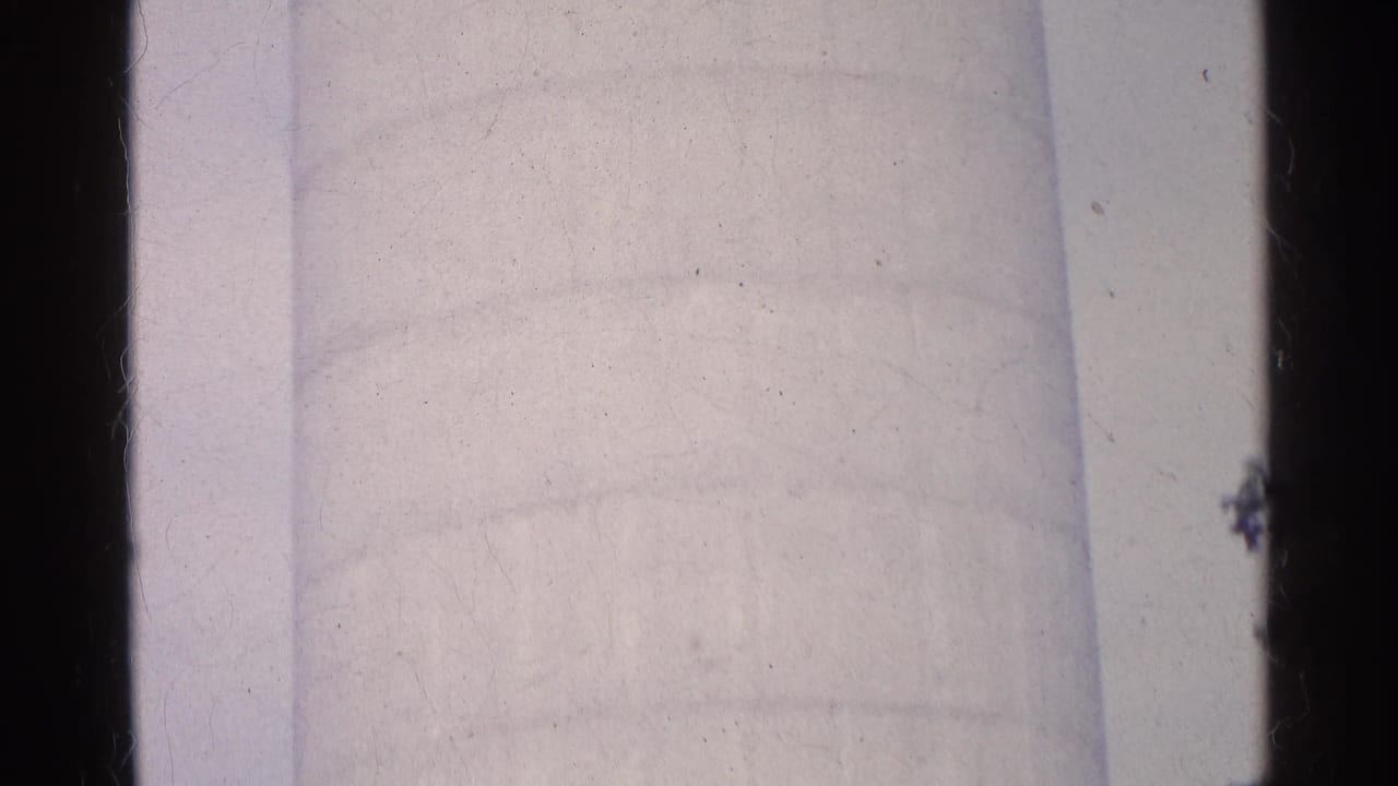 1961 Swiss home-movie frame with the silo partly obscured by dark frame edge and treetop silhouettes against the sky.