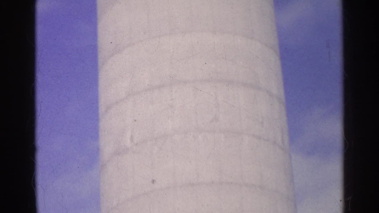 1961 Swiss 8mm frame showing the white cylindrical silo against blue sky, with cloudy patches and dark film borders.
