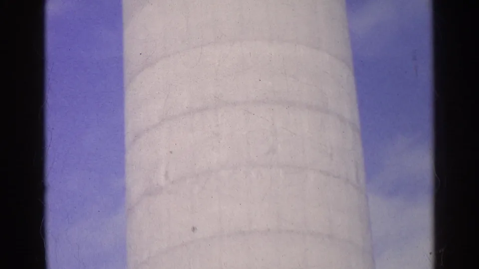 1961 Swiss 8mm frame showing the white cylindrical silo against blue sky, with cloudy patches and dark film borders.