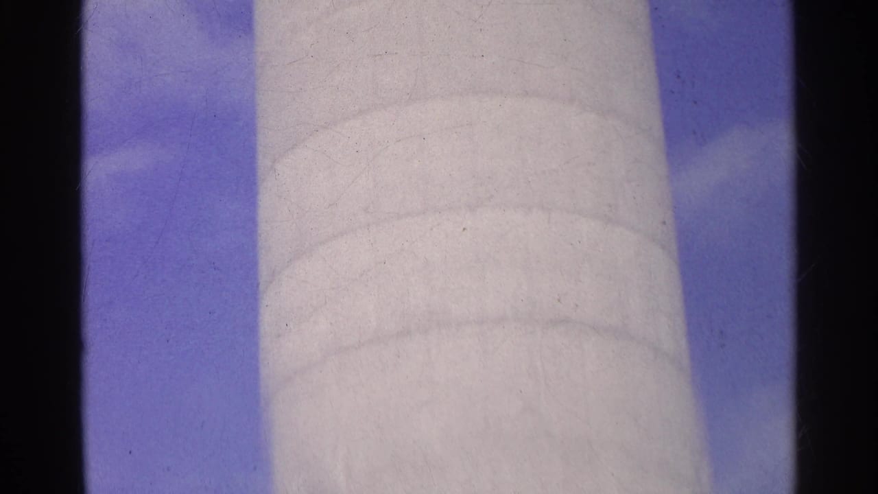 1961 Switzerland 8mm frame showing a pale cylindrical tower or column viewed upward against blue sky and clouds.