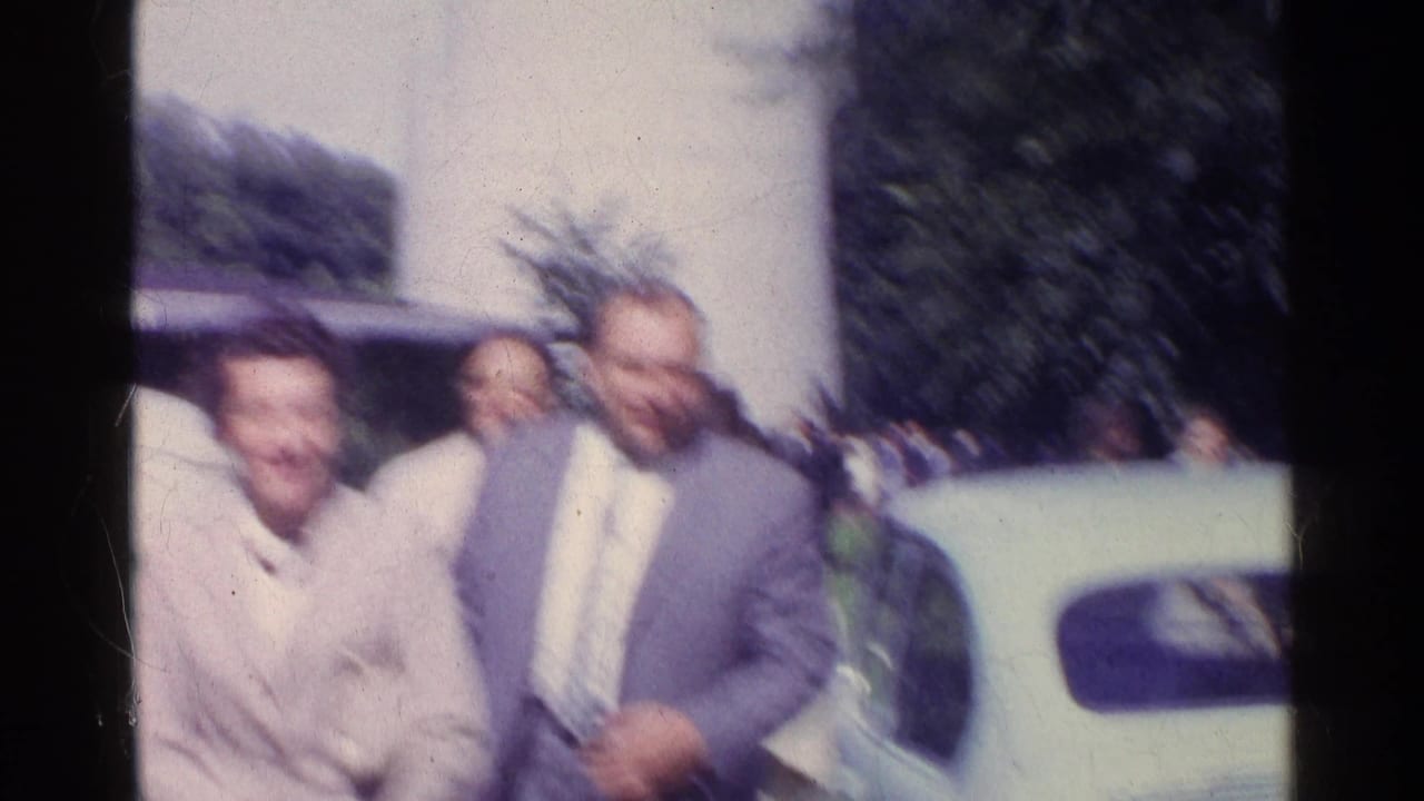 Blurry 1961 Switzerland home-movie view of suited men near the TV tower, with trees and a pale car in the background.