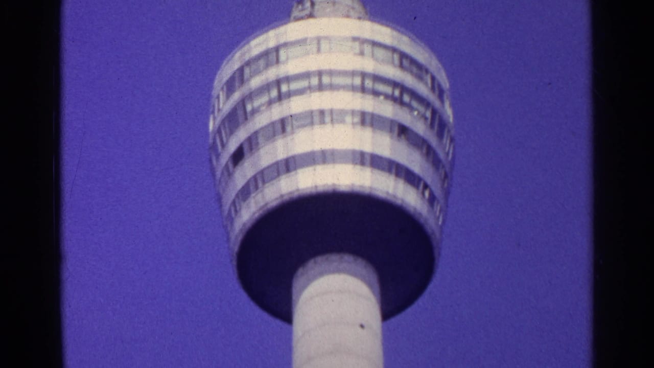 Low-angle 1961 Switzerland home-movie view of a tall cylindrical modern tower against a blue-purple sky.