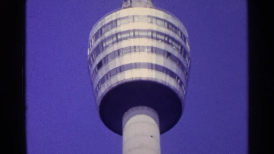 Low-angle 1961 Switzerland home-movie view of a tall cylindrical modern tower against a blue-purple sky.