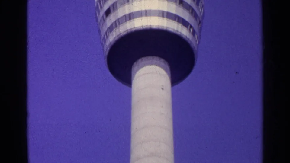 The observation tower fills the upper frame, with its rounded deck, railing bands, and pale shaft seen from below in Swiss 1961 footage.