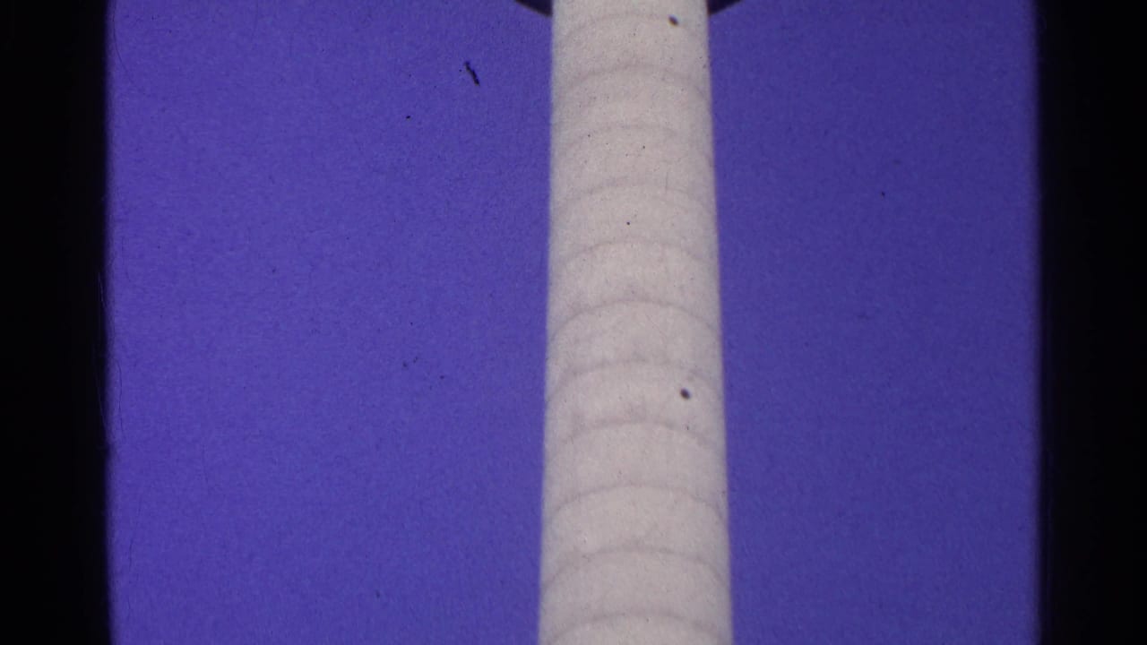 A vertical section of the observation tower's pale shaft stands against a deep blue sky, with visible 8mm frame borders and grain.
