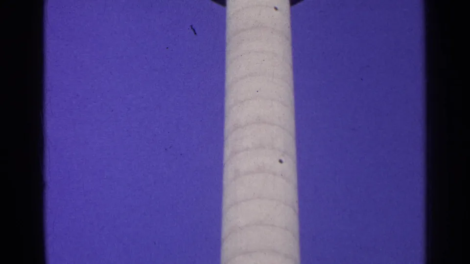 A vertical section of the observation tower's pale shaft stands against a deep blue sky, with visible 8mm frame borders and grain.