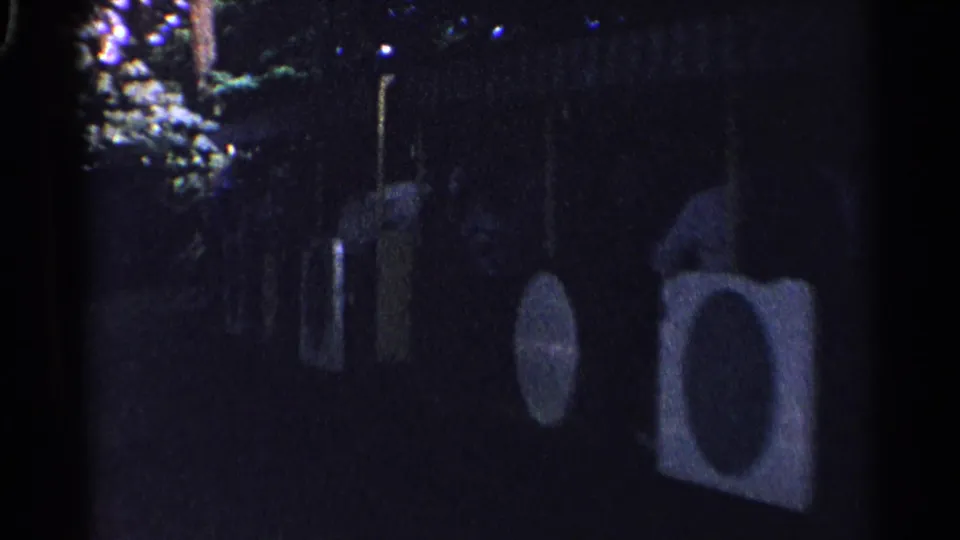 1961 Switzerland 8mm frame showing a dim nighttime outdoor area with circular decorations or targets near trees.