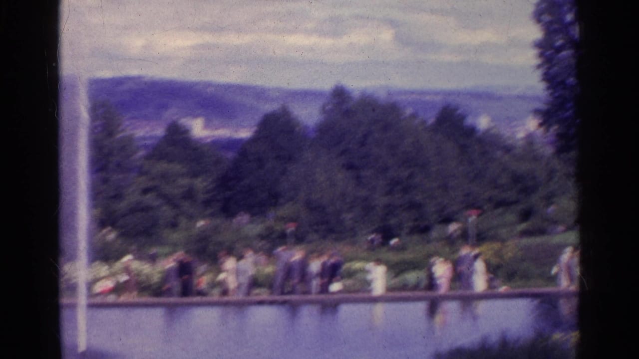 Fountain and pond with people walking along a garden path under trees.