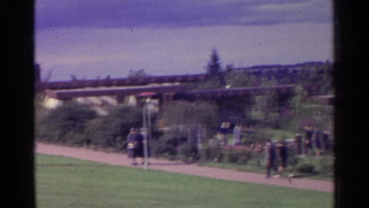 Small groups of people walking near garden beds and a low modernist structure.