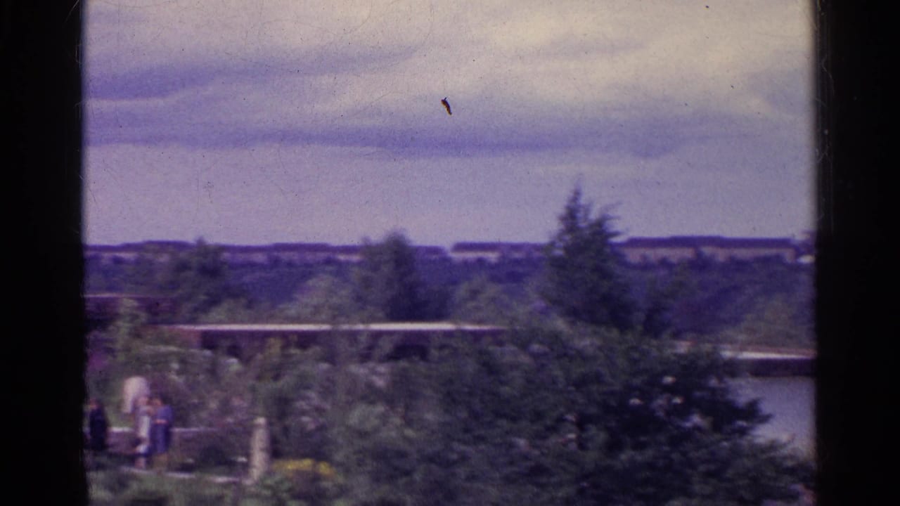 1961 Switzerland 8mm frame showing a distant wooded compound, low modernist buildings, and small figures near garden paths.