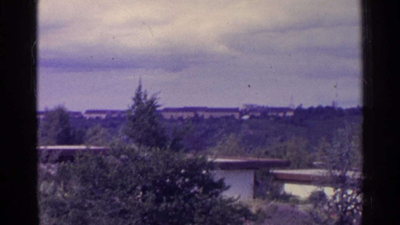 Panoramic view across trees and low buildings framed by dark film borders.