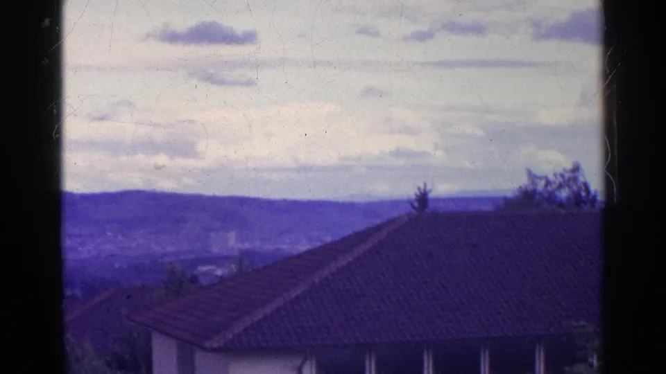 1961 Swiss town overlook with a tiled roof in front, valley detail below, distant hills, and aged blue-purple color.