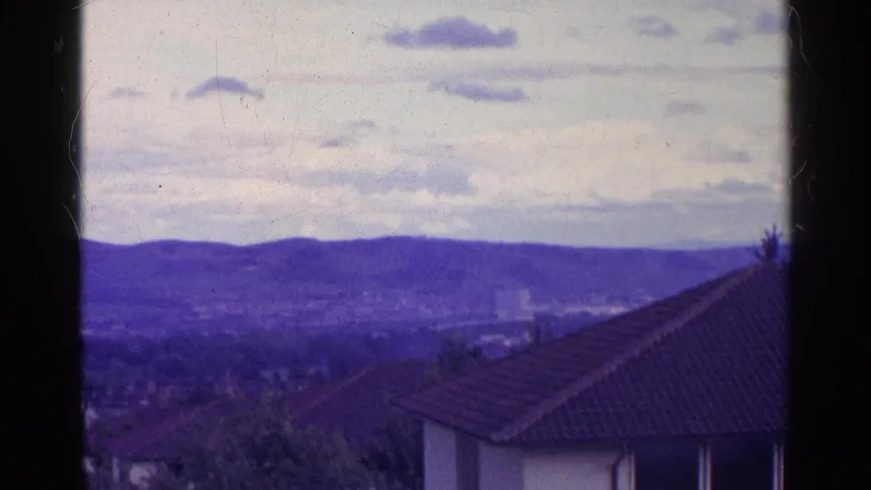 1961 Swiss 8mm frame showing a hazy town and tiled roof beneath purple-blue mountains, bordered by dark film edges.