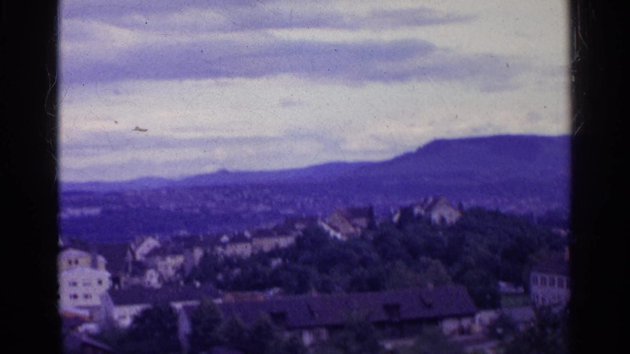 Town rooftops and trees seen from above with a broad mountain ridge in the distance.