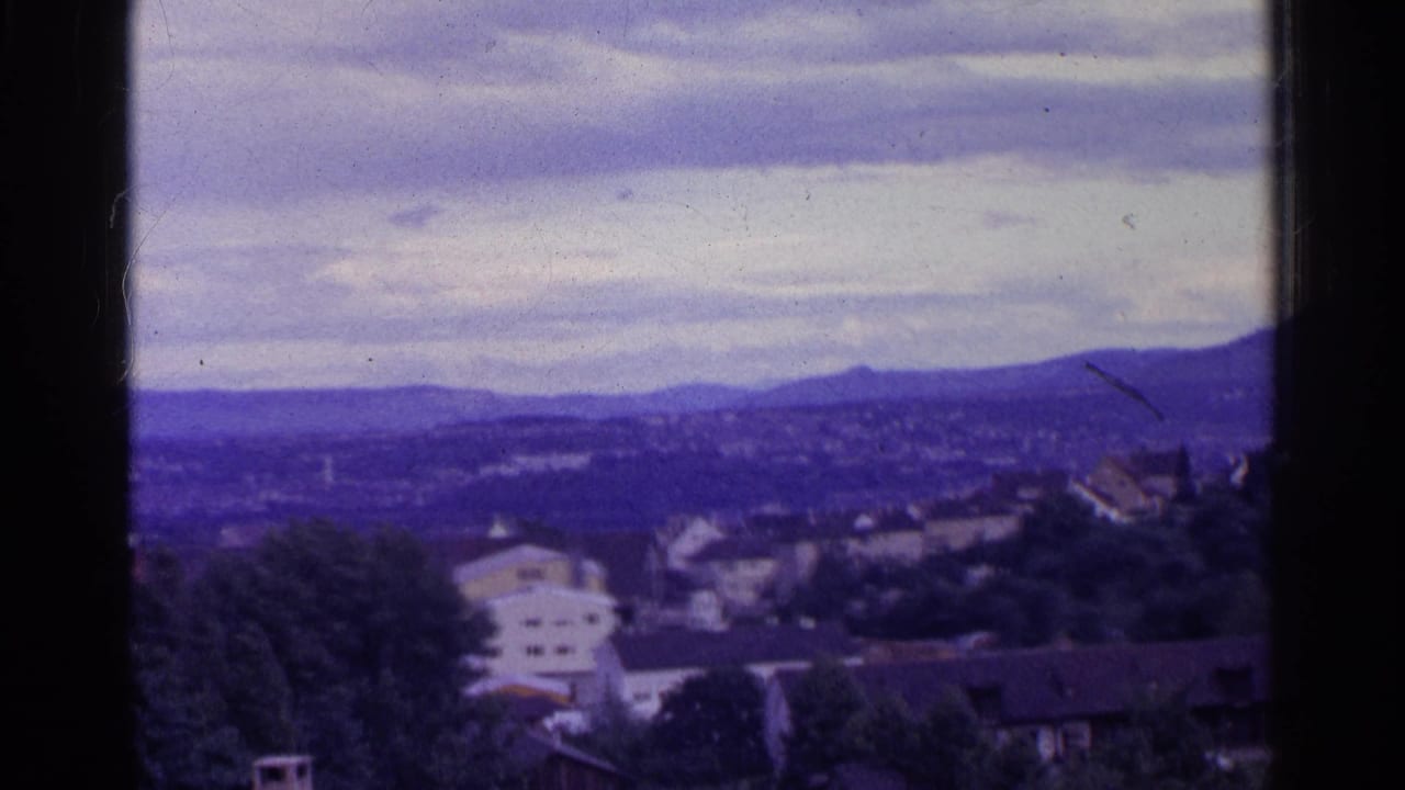1961 Swiss 8mm frame with soft-focus houses, treetops, rolling hills, and a muted cloudy sky.