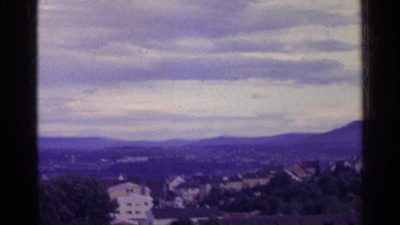 Swiss valley panorama from 1961 with rooftops, distant hills, layered clouds, and a dark vertical border crossing the view.