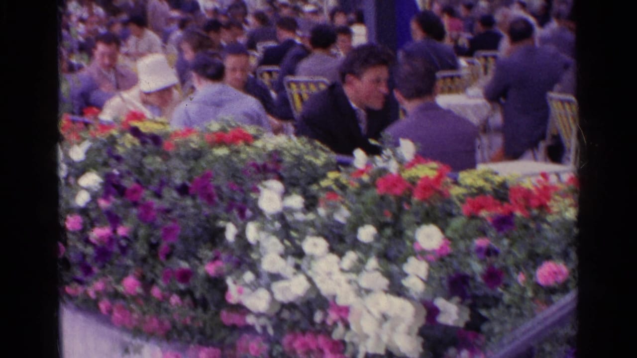 Flower-filled concrete planter in front of seated adults at an outdoor gathering.