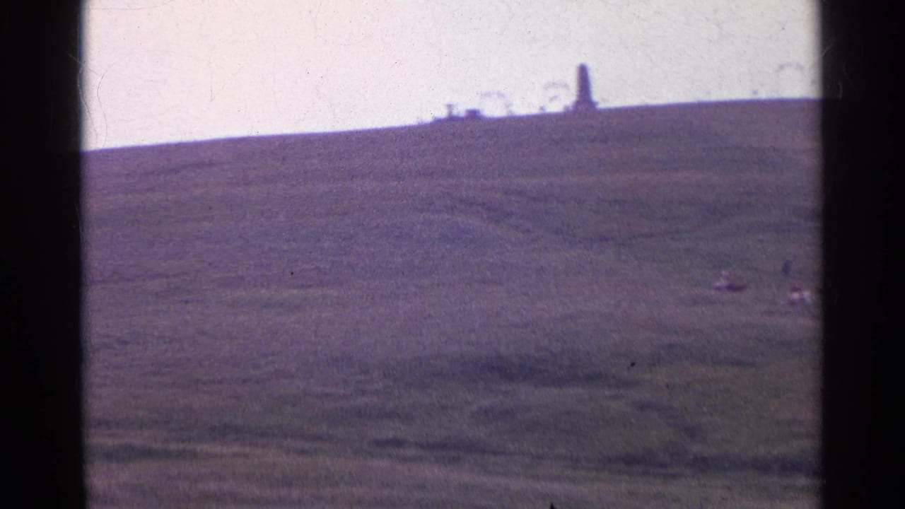 1961 Swiss 8mm frame showing a soft, distant ridge-top tower above rolling short-grass hills.