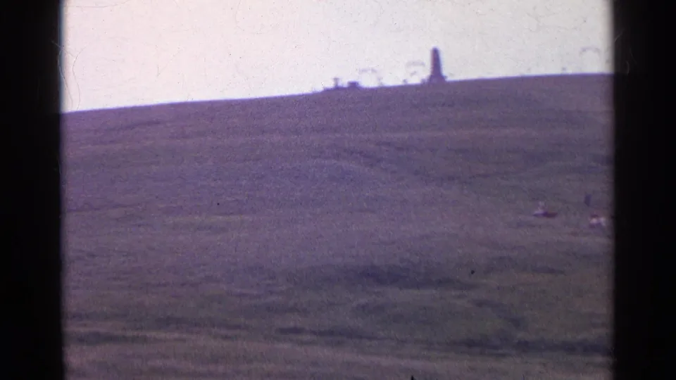 1961 Swiss 8mm frame showing a soft, distant ridge-top tower above rolling short-grass hills.