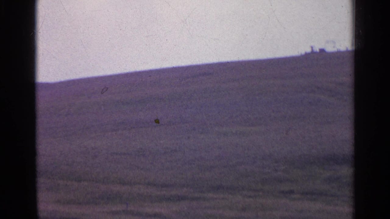 Open grassy hillside and ridge line, with distant shapes near the horizon.